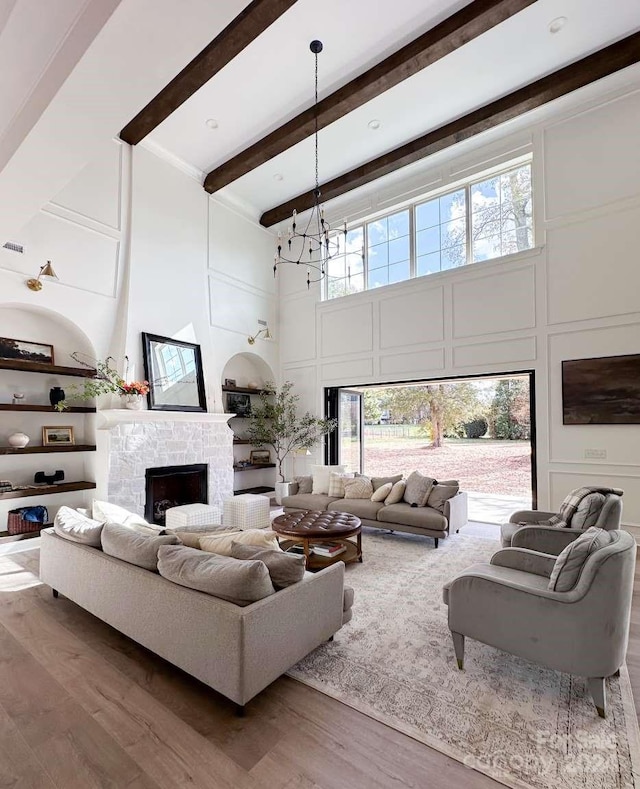 living room with hardwood / wood-style flooring, beam ceiling, a chandelier, a fireplace, and a towering ceiling