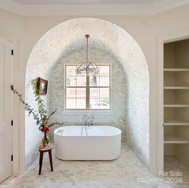 bathroom with brick wall, vaulted ceiling, a bathing tub, a chandelier, and built in shelves