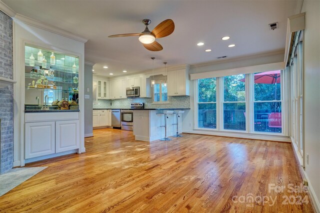 kitchen with hanging light fixtures, stainless steel appliances, ornamental molding, light wood-type flooring, and white cabinetry