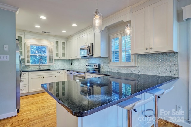 kitchen with kitchen peninsula, hanging light fixtures, white cabinetry, stainless steel appliances, and a breakfast bar