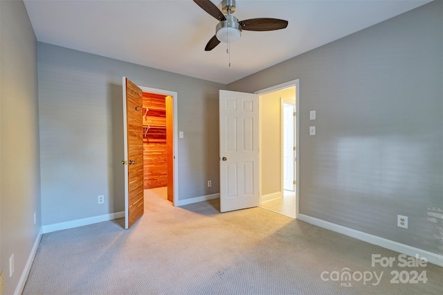 unfurnished bedroom with a spacious closet, light carpet, a closet, and ceiling fan