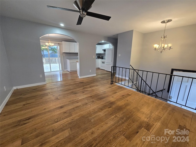 unfurnished living room featuring wood-type flooring and ceiling fan with notable chandelier