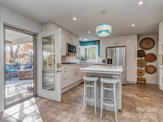 kitchen featuring white cabinetry, pendant lighting, decorative backsplash, a kitchen island, and appliances with stainless steel finishes