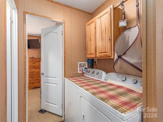 clothes washing area featuring a textured ceiling, light carpet, washing machine and dryer, and cabinets