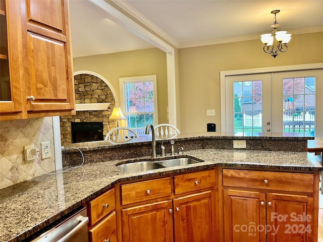 kitchen with sink, stainless steel dishwasher, crown molding, dark stone counters, and a fireplace