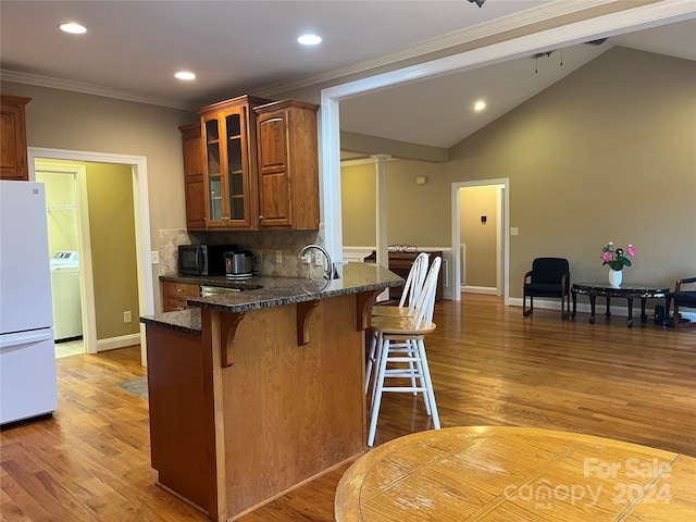 kitchen featuring a breakfast bar, hardwood / wood-style floors, washer / dryer, white fridge, and lofted ceiling