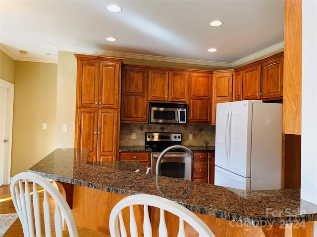 kitchen featuring kitchen peninsula, appliances with stainless steel finishes, ornamental molding, dark stone countertops, and hardwood / wood-style floors