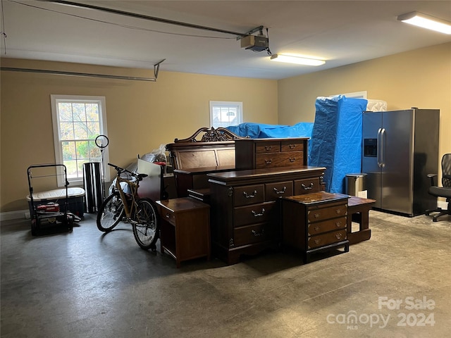 garage with a garage door opener and stainless steel refrigerator with ice dispenser