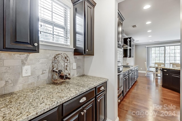 kitchen with stainless steel appliances, dark brown cabinetry, light stone countertops, light wood-type flooring, and decorative backsplash