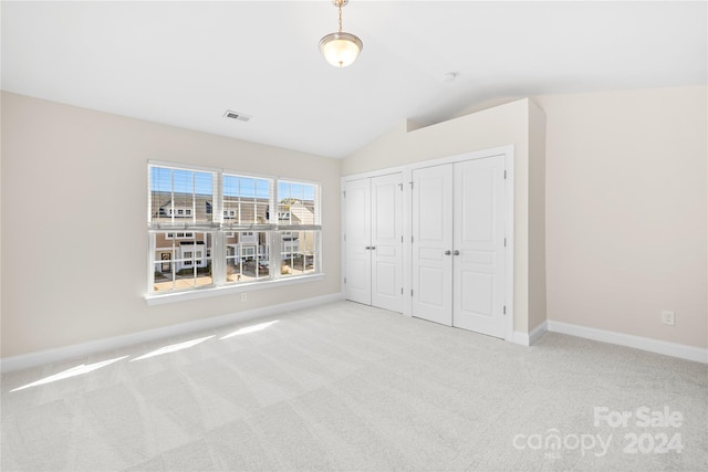 unfurnished bedroom featuring light carpet, multiple closets, and vaulted ceiling