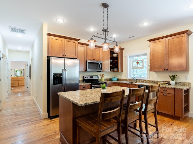 kitchen with light hardwood / wood-style floors, stainless steel appliances, a kitchen island, and hanging light fixtures