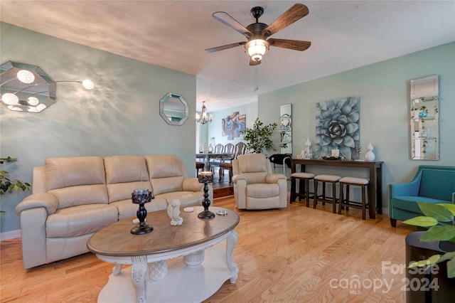 living room with ceiling fan with notable chandelier, light hardwood / wood-style floors, and a textured ceiling