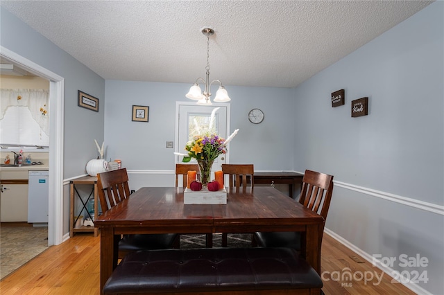 dining space with a notable chandelier, a textured ceiling, sink, and light wood-type flooring