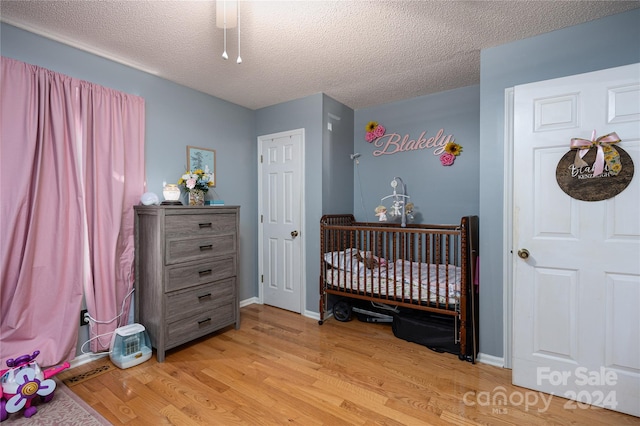 bedroom with a nursery area, a textured ceiling, light wood-type flooring, and ceiling fan