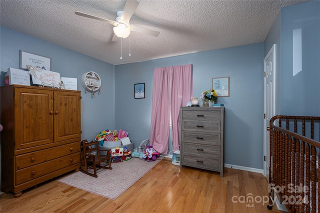 bedroom featuring light hardwood / wood-style floors, a textured ceiling, a crib, and ceiling fan