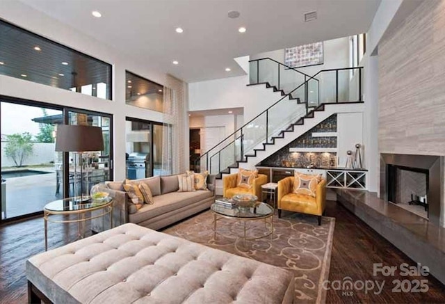 living room with stairway, recessed lighting, a fireplace, a high ceiling, and wood finished floors