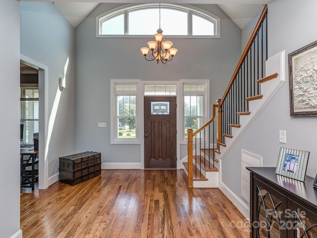 foyer entrance featuring high vaulted ceiling, wood-type flooring, a wealth of natural light, and a chandelier