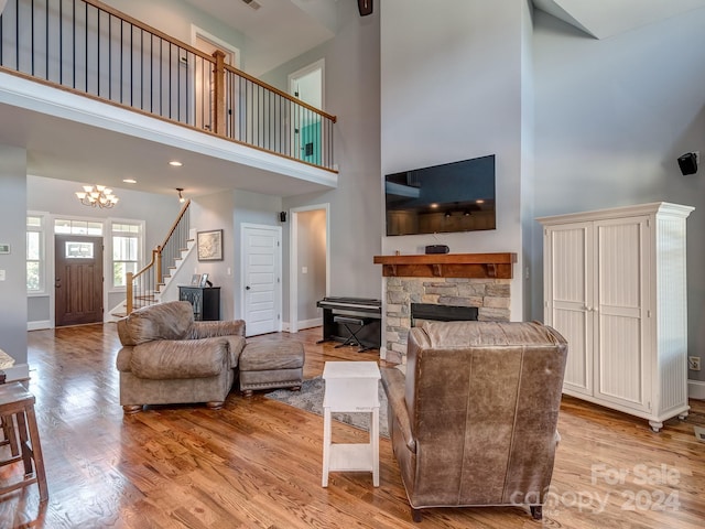 living room featuring a towering ceiling, an inviting chandelier, a stone fireplace, and light wood-type flooring