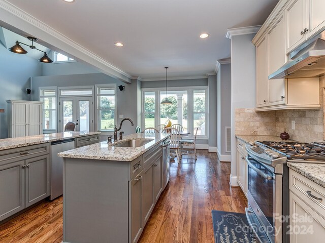 kitchen featuring an island with sink, wood-type flooring, ornamental molding, sink, and appliances with stainless steel finishes