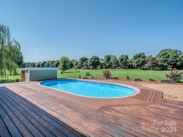 view of pool with a deck, a lawn, and an outdoor structure