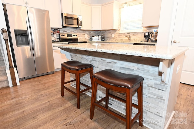 kitchen with a kitchen island, light stone counters, stainless steel appliances, and light wood-type flooring