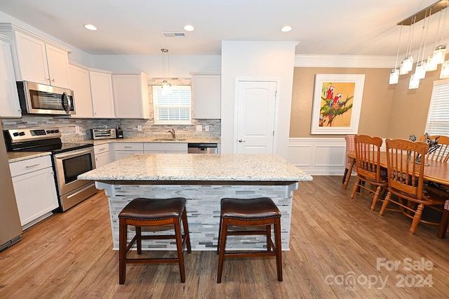 kitchen with appliances with stainless steel finishes, decorative light fixtures, light wood-type flooring, and a kitchen island