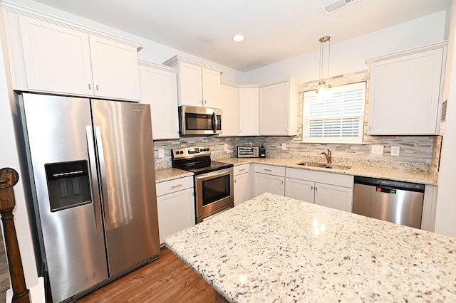 kitchen with sink, backsplash, light hardwood / wood-style floors, stainless steel appliances, and pendant lighting