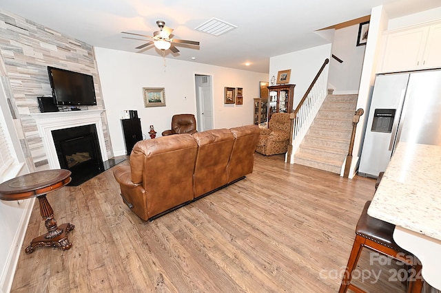 living room featuring a large fireplace, light wood-type flooring, and ceiling fan