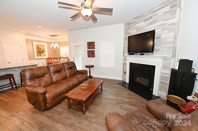 living room featuring a large fireplace, wood-type flooring, and ceiling fan with notable chandelier