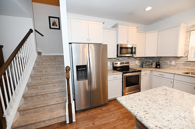 kitchen featuring white cabinetry, light stone countertops, appliances with stainless steel finishes, and light hardwood / wood-style flooring