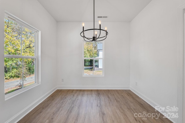 unfurnished dining area with a chandelier, a wealth of natural light, and light wood-type flooring