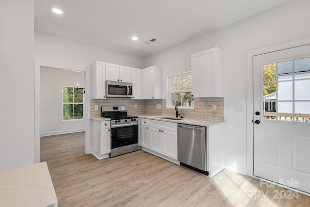 kitchen with white cabinets, a healthy amount of sunlight, appliances with stainless steel finishes, light wood-type flooring, and sink