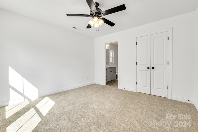 unfurnished bedroom featuring a closet, ceiling fan, light colored carpet, and ensuite bath