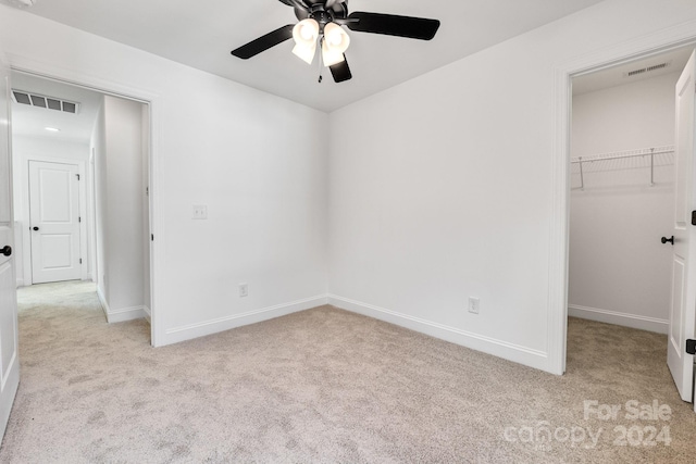 unfurnished bedroom with a spacious closet, light carpet, a closet, and ceiling fan