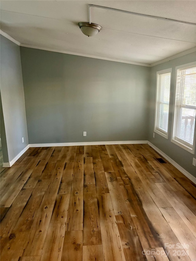 empty room with hardwood / wood-style floors and crown molding