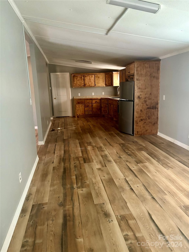 kitchen featuring stainless steel fridge, crown molding, sink, vaulted ceiling, and light hardwood / wood-style floors