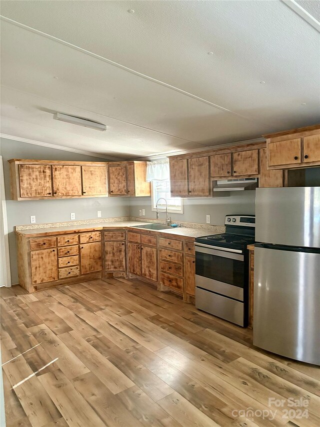 kitchen featuring sink, appliances with stainless steel finishes, a textured ceiling, light wood-type flooring, and vaulted ceiling