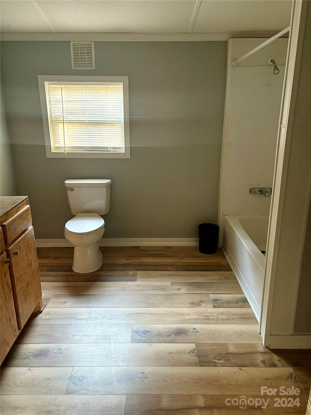 full bathroom with hardwood / wood-style floors, washtub / shower combination, vanity, and toilet