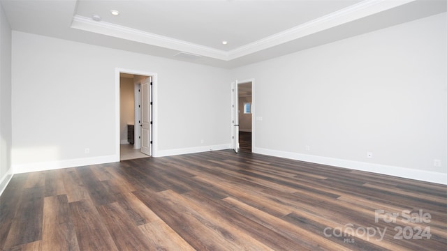 empty room featuring a raised ceiling, dark hardwood / wood-style flooring, and ornamental molding