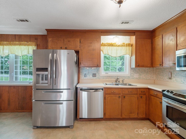 kitchen featuring stainless steel appliances, sink, a textured ceiling, and wood walls