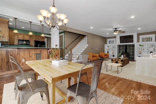 dining room with ceiling fan with notable chandelier, a wood stove, and light hardwood / wood-style flooring