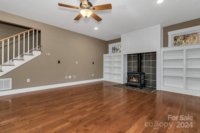 unfurnished living room with a wood stove, ceiling fan, built in features, and hardwood / wood-style flooring