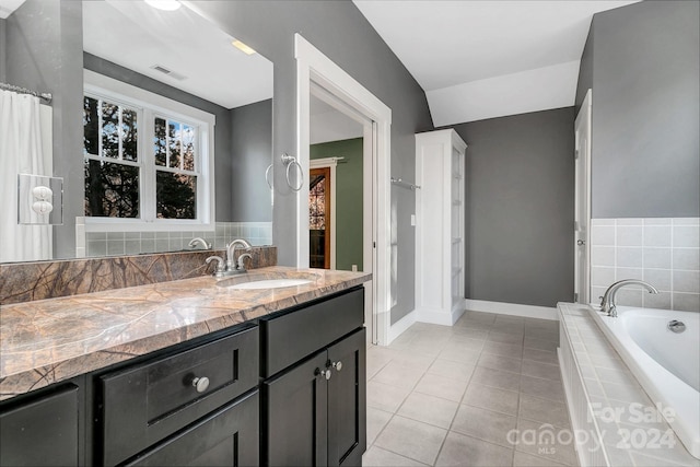 bathroom with tiled bath, tile patterned flooring, vanity, and lofted ceiling