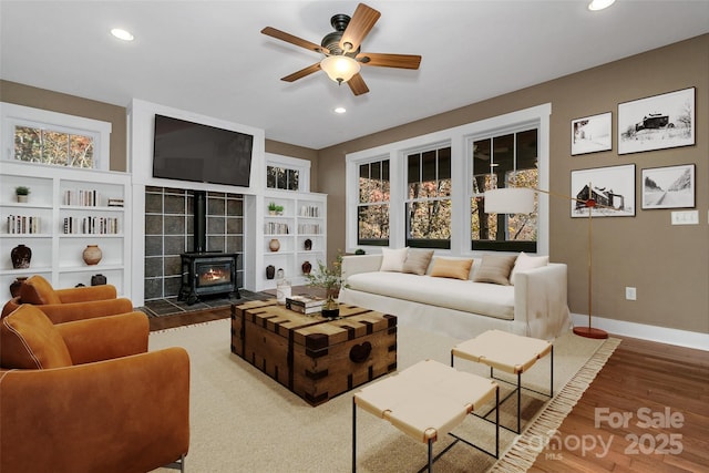 living area with baseboards, a ceiling fan, a wood stove, and recessed lighting