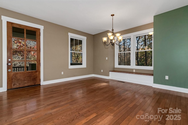 spare room with a notable chandelier, baseboards, dark wood-style flooring, and visible vents