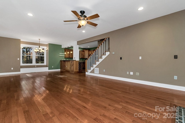 unfurnished living room featuring stairway, ceiling fan with notable chandelier, dark wood finished floors, baseboards, and recessed lighting