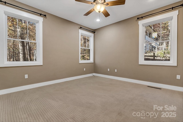 carpeted empty room with baseboards, a ceiling fan, and visible vents