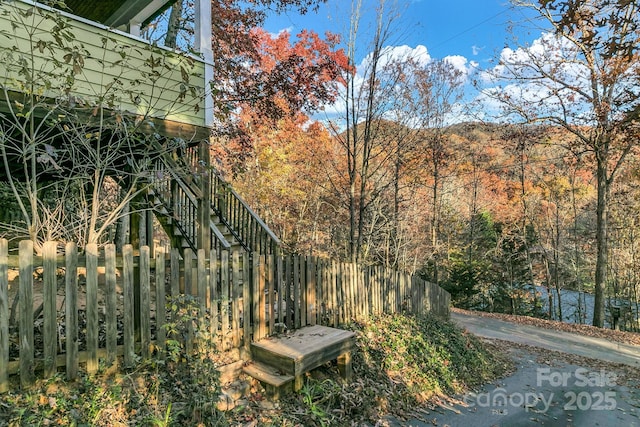 view of yard featuring a wooded view, stairs, and fence