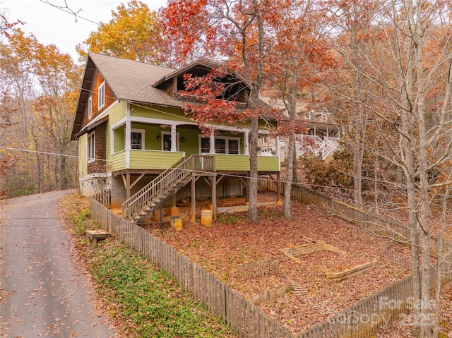 view of front of property featuring aphalt driveway, stairs, fence, a shingled roof, and a porch