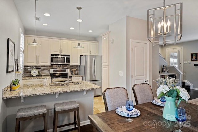 kitchen with tasteful backsplash, hanging light fixtures, stainless steel appliances, and light stone countertops